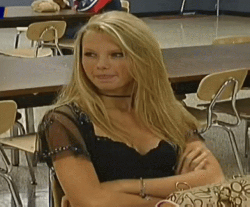 A Woman In A Black Top Is Sitting At A Table With Her Arms Crossed GIF