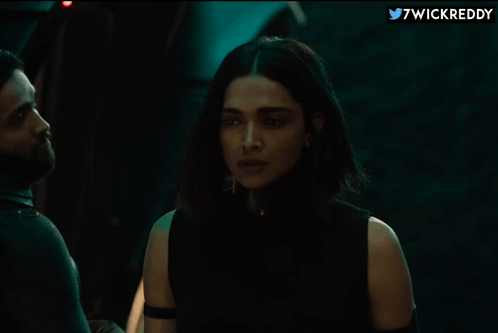 A Woman In A Black Top Is Standing Next To A Man In A Dark Room With 7Wickreddy Written On The Bottom GIF