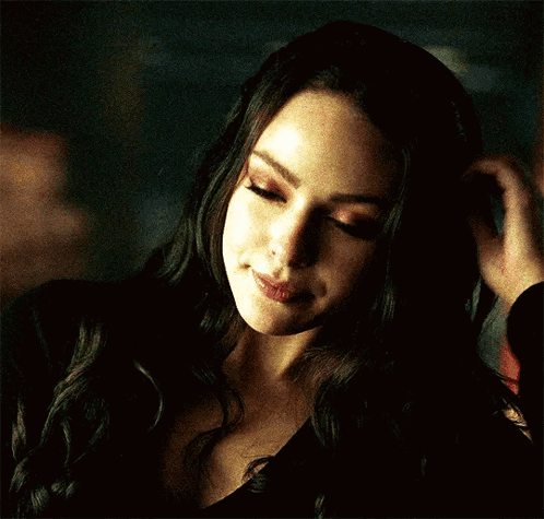 A Woman In A Black Top Is Touching Her Hair GIF