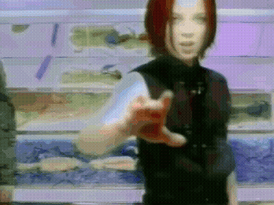A Woman In A Black Vest Is Pointing At The Camera GIF