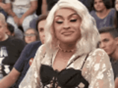 A Woman In A Blonde Wig Is Sitting In A Crowd Of People . GIF