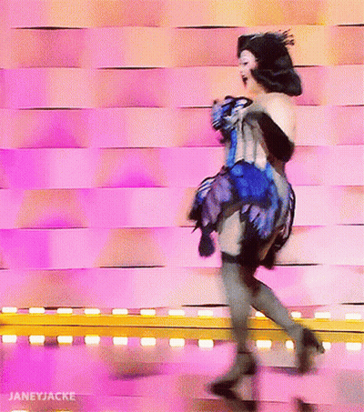 A Woman In A Blue And Black Dress Is Dancing In Front Of A Pink Wall With Janeyjacke Written On The Bottom GIF