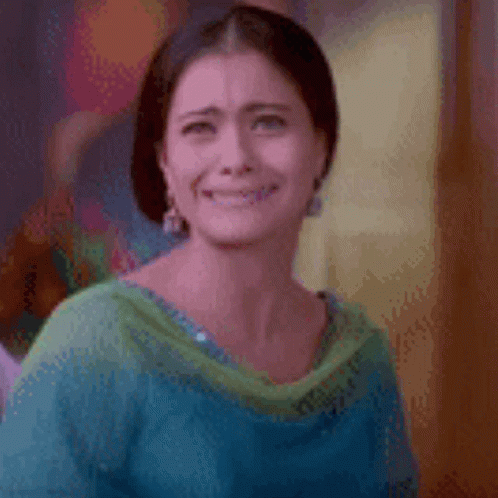 A Woman In A Blue And Green Dress Is Smiling And Making A Funny Face . GIF