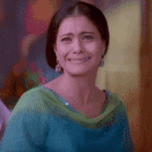 A Woman In A Blue And Green Shirt Is Smiling And Making A Funny Face . GIF