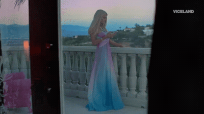 A Woman In A Blue And Pink Dress Is Standing On A Balcony With The Word Viceland On The Bottom Right GIF