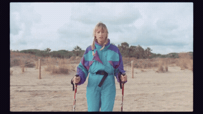 A Woman In A Blue And Purple Ski Suit Holds Walking Poles GIF