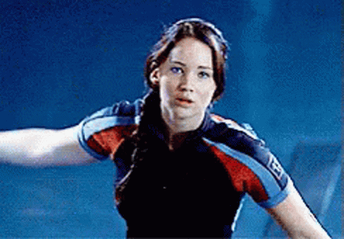 A Woman In A Blue And Red Shirt Is Standing In A Dark Room . GIF