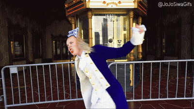A Woman In A Blue And White Costume Is Standing In Front Of A Fence With The Number 6030 On It GIF