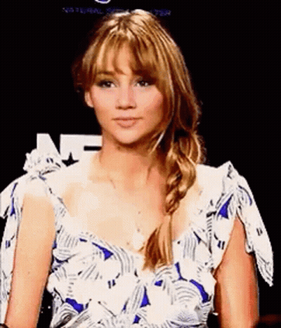 A Woman In A Blue And White Dress Is Sitting In Front Of A Black Background . GIF