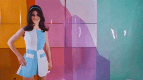 A Woman In A Blue And White Dress Is Standing In Front Of A Colorful Wall With A Hole In It . GIF