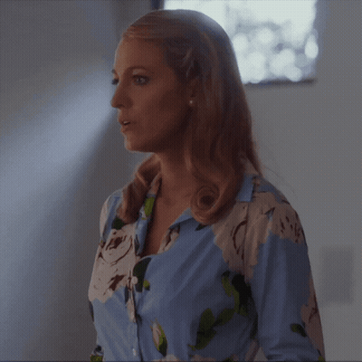 A Woman In A Blue And White Floral Shirt Is Standing In Front Of A Window GIF