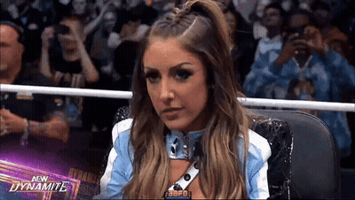 A Woman In A Blue And White Jacket Is Sitting In A Wrestling Ring In Front Of A Crowd . GIF