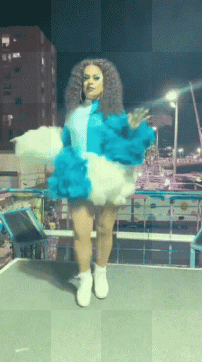 A Woman In A Blue And White Outfit Is Standing On A Stage GIF