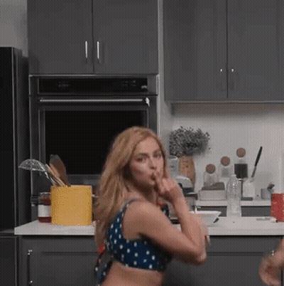 A Woman In A Blue And White Polka Dot Top Stands In A Kitchen GIF