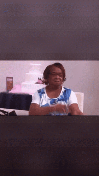 A Woman In A Blue And White Shirt Is Sitting At A Table In Front Of A Wedding Cake . GIF