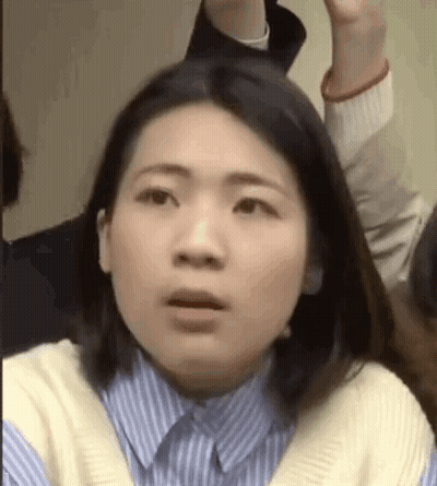 A Woman In A Blue And White Striped Shirt Is Making A Funny Face While Sitting In A Crowd . GIF