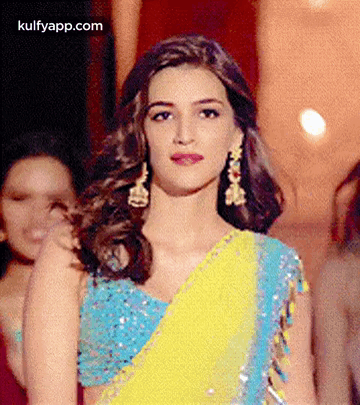 A Woman In A Blue And Yellow Saree Is Standing In Front Of A Group Of Women . GIF
