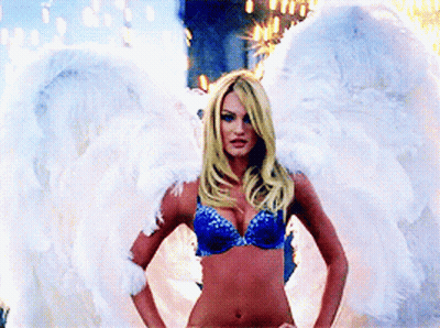 A Woman In A Blue Bra And White Angel Wings Stands With Her Hands On Her Hips GIF