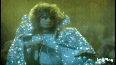 A Woman In A Blue Cape Is Singing Into A Microphone On Stage . GIF