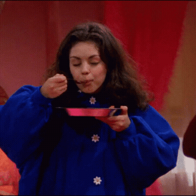 A Woman In A Blue Coat Is Holding A Fork And A Plate Of Food . GIF