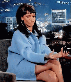 A Woman In A Blue Coat Is Sitting On A Couch In Front Of A Hollywood Sign GIF