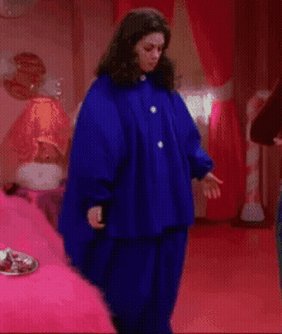 A Woman In A Blue Coat Is Standing In A Bedroom GIF