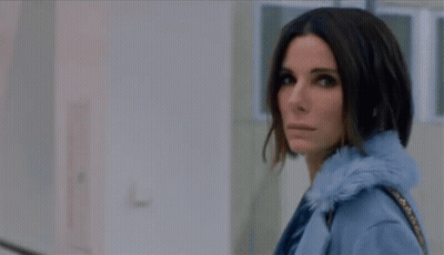 A Woman In A Blue Coat Is Standing In A Hallway Looking At The Camera GIF
