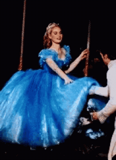 A Woman In A Blue Dress Is Being Helped Up By A Man In A White Suit . GIF