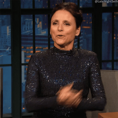 A Woman In A Blue Dress Is Clapping Her Hands In Front Of A Large Window GIF