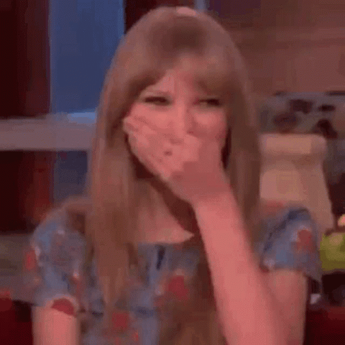 A Woman In A Blue Dress Is Covering Her Mouth With Her Hand . GIF