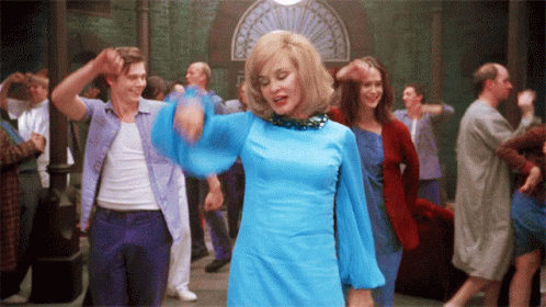 A Woman In A Blue Dress Is Dancing In A Crowded Room GIF