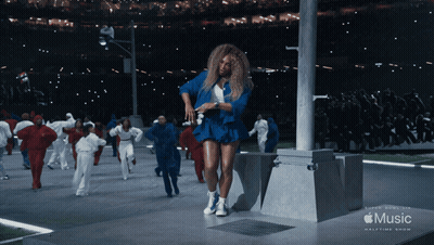 A Woman In A Blue Dress Is Dancing In Front Of A Music Halftime Show Banner GIF