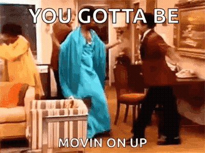 A Woman In A Blue Dress Is Dancing With A Man In A Suit In A Living Room . GIF