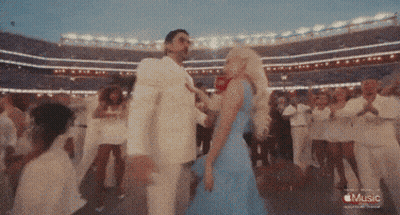 A Woman In A Blue Dress Is Dancing With A Man In A White Suit In A Stadium With The Words Music On The Bottom GIF