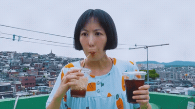 A Woman In A Blue Dress Is Drinking From A Plastic Cup GIF