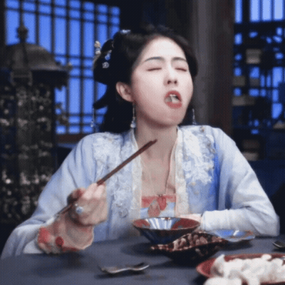 A Woman In A Blue Dress Is Eating Food With Chopsticks GIF