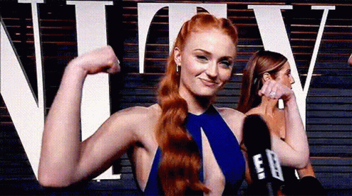 A Woman In A Blue Dress Is Flexing Her Muscles In Front Of A Microphone . GIF