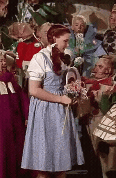 A Woman In A Blue Dress Is Holding A Basket Of Flowers GIF