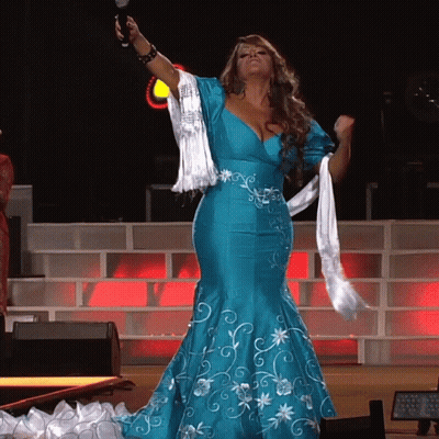 A Woman In A Blue Dress Is Holding A Microphone In Her Hand GIF