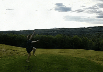A Woman In A Blue Dress Is Jumping In The Air In A Grassy Field GIF