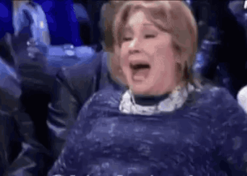 A Woman In A Blue Dress Is Laughing With Her Mouth Open . GIF