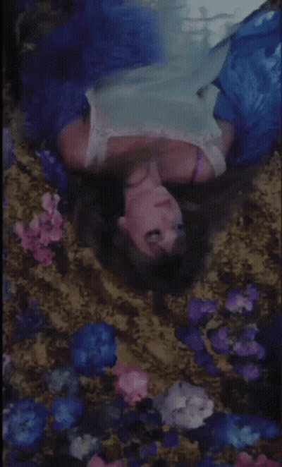 A Woman In A Blue Dress Is Laying In A Bed Of Flowers . GIF