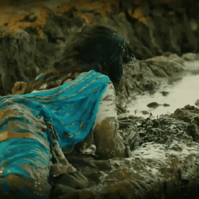 A Woman In A Blue Dress Is Laying In The Mud On The Beach GIF