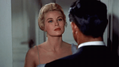 A Woman In A Blue Dress Is Looking At Herself In A Mirror While A Man In A Suit Looks On . GIF