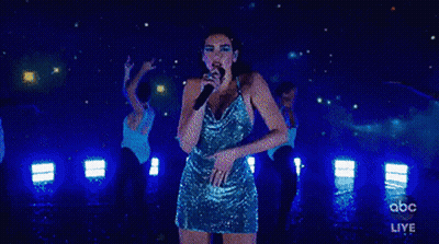 A Woman In A Blue Dress Is Singing Into A Microphone On Stage . GIF