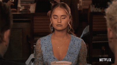 A Woman In A Blue Dress Is Sitting At A Table With A Netflix Logo In The Corner GIF