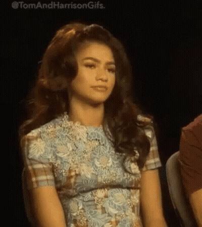 A Woman In A Blue Dress Is Sitting In A Chair And Looking At The Camera . GIF