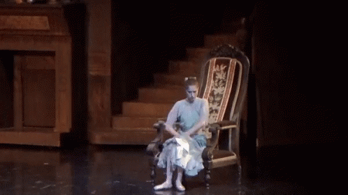 A Woman In A Blue Dress Is Sitting In A Chair On A Stage GIF