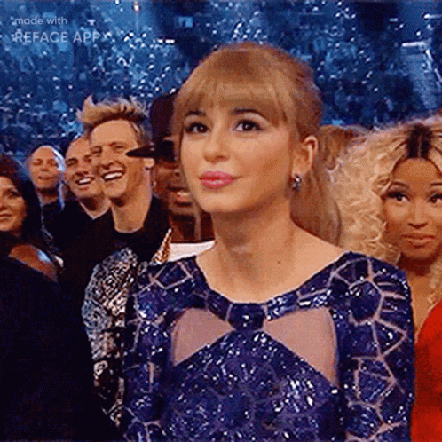 A Woman In A Blue Dress Is Sitting In Front Of A Crowd Of People . GIF