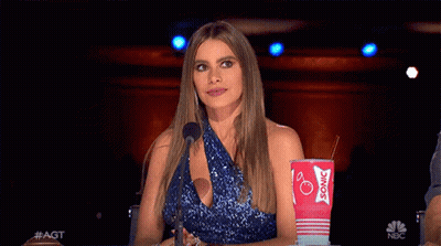 A Woman In A Blue Dress Is Sitting In Front Of A Microphone Holding A Sonic Cup GIF